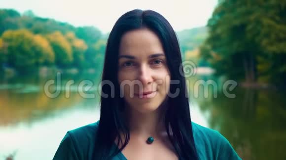一个年轻微笑的黑发女人的肖像一个有酒窝的女孩一天日落时靠近湖边的女人视频的预览图