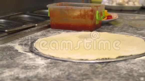 厨师把红色的番茄酱倒入卷好的面团上在咖啡馆的厨房里做披萨的过程视频的预览图