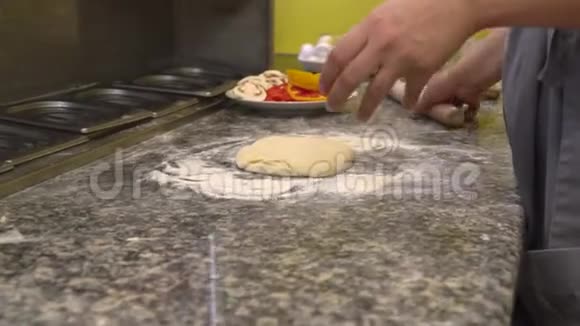 厨师用擀面杖把面团擀成比萨饼有一个盘子上面有切碎的辣椒西红柿和蘑菇视频的预览图