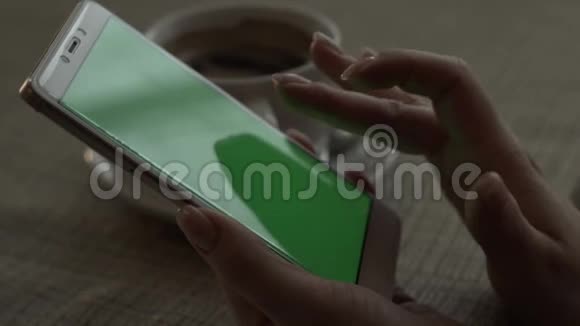 女人手在背景咖啡杯上触摸绿色屏幕手机视频的预览图