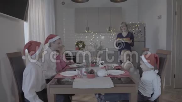 快乐的六个兴奋的家庭享受节日的圣诞晚餐在可爱舒适的厨房庆祝活动臂圈戴着圣诞帽视频的预览图