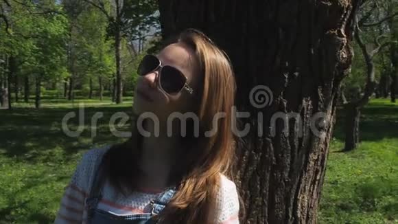 公园里戴太阳镜的漂亮女孩少女特写自然在阳光明媚的日子里戴雀斑和眼镜的女孩视频的预览图