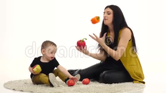 妈妈和孩子坐在地板上周围有很多蔬菜和水果白色背景视频的预览图