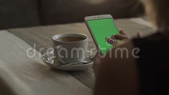 女人手在背景咖啡杯上触摸绿色屏幕手机视频的预览图