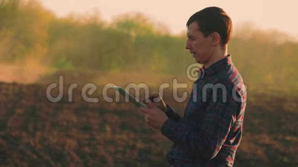 年轻的农民在田间拖拉机前拿着平板电脑季节性农业工人概念生态运输视频的预览图