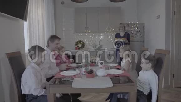 令人兴奋的六人幸福的家庭在可爱舒适的厨房庆祝活动中享受圣诞晚餐戴上圣诞帽视频的预览图