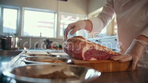 屠夫将香料加入到一大块新鲜的生肉中放在商业厨房的木板上动作缓慢视频的预览图