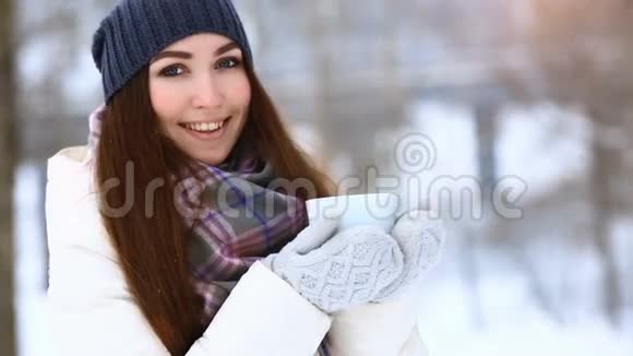 美丽欢乐的模特女孩拿着杯子喝着热茶微笑着在冬天的公园里玩得很开心美丽的年轻女子在户外笑视频的预览图