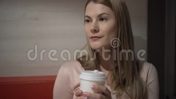 美丽迷人的年轻女人在咖啡馆里喝咖啡晚上好纸咖啡杯红色沙发视频的预览图