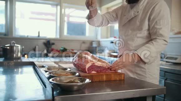 屠夫将香料加入到一大块新鲜的生肉中放在商业厨房的木板上动作缓慢视频的预览图