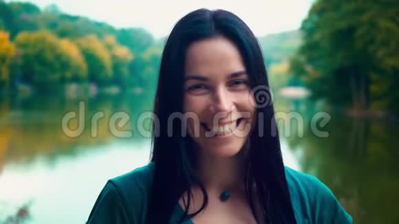 一个年轻微笑的黑发女人的肖像一个有酒窝的女孩一天日落时靠近湖边的女人视频的预览图