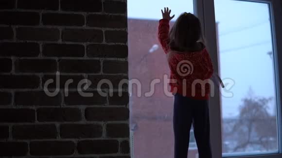 小可爱的女孩站在窗台上望着外面的雪城风景视频的预览图
