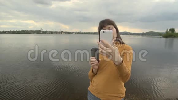 一个年轻的女人在一个城市池塘旁边的电话上拍了一幅自画像视频的预览图