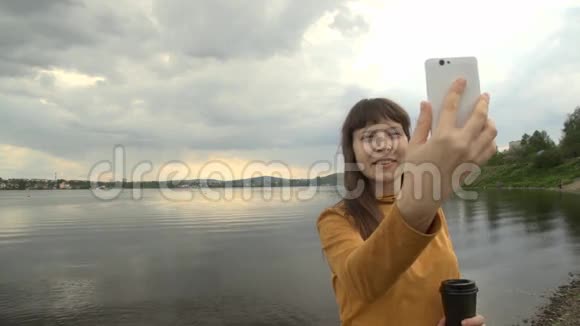 一个年轻的女人在一个城市池塘旁边的电话上拍了一幅自画像视频的预览图