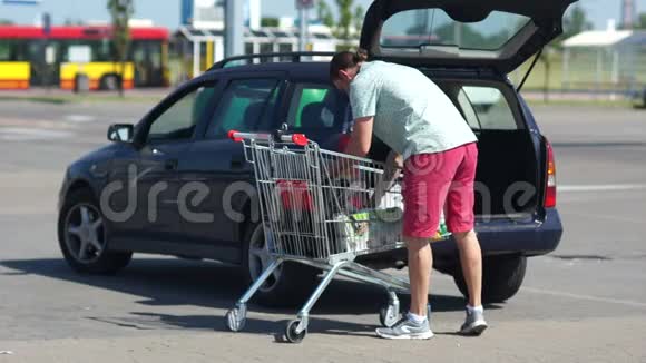 一个男人在停车场把食物从购物车装进后备箱男人在家庭中的作用分布情况视频的预览图