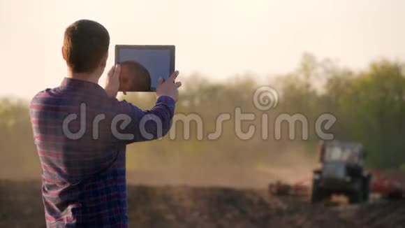 年轻的农民在田间拖拉机前拿着平板电脑季节性农业工人概念生态运输视频的预览图