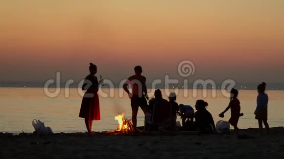 海边的剪影一个大家庭在火附近的海边休息人们在火灾后休息视频的预览图