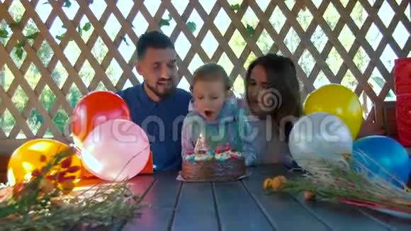 小女孩和父母坐在一起在生日蛋糕上吹蜡烛视频的预览图