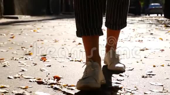 慢动作女孩在橙色叶子上的秋天公园里散步粉碎的采摘叶秋天白色运动鞋的方法视频的预览图