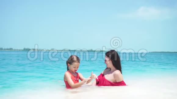 热带海滩上可爱的小女孩和年轻的妈妈躺在白色沙滩上享受他们的暑假视频的预览图