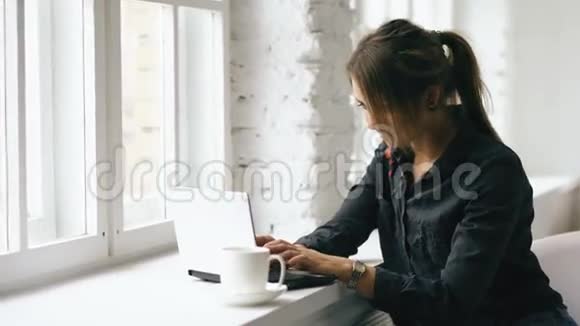 年轻微笑的女学生坐在咖啡店的桌子上手提电脑在室内视频的预览图