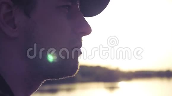 年轻的帅哥坐在湖岸的侧面背景是夕阳特写镜头慢速全高清1080p视频的预览图
