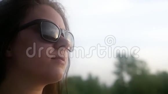 美丽的年轻女子透过眼镜看着太阳在日落的天空中1920x1080高清视频的预览图
