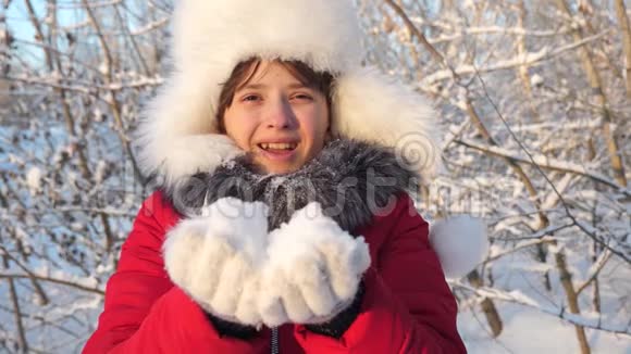 快乐的女孩在日落时吹雪花在冬天的公园里微笑慢动作3小女孩从身上掉下雪花视频的预览图
