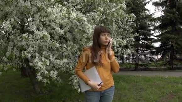 女人在电话里拿着文件工作旁边是盛开的苹果树视频的预览图