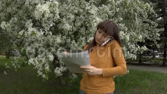 女人在电话里拿着文件工作旁边是盛开的苹果树视频的预览图