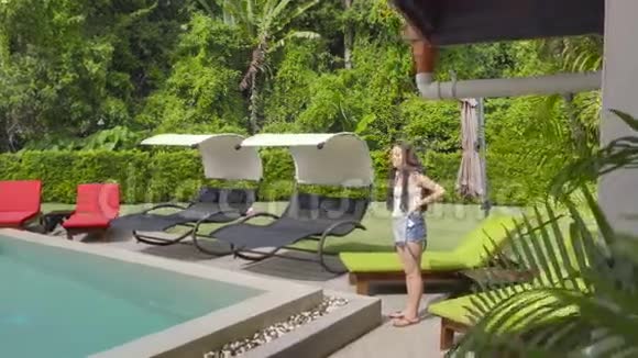 年轻漂亮的女人带着非洲编织的日光浴和沿着游泳池散步视频的预览图