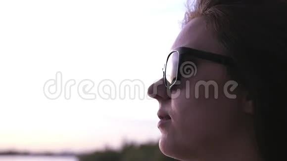 一个年轻漂亮的女孩站在海滨戴着太阳镜欣赏日落戴上帽子慢动作1920x1080视频的预览图
