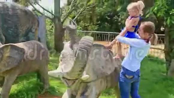 母亲在公园的大象雕像上坐小金发女孩视频的预览图