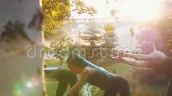 两名年轻女性在阳光下和教练一起在公园里做瑜伽练习一名女性长着蓝色的恐惧症视频的预览图