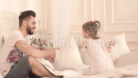 快乐的父亲和他的小女儿在床上玩视频的预览图
