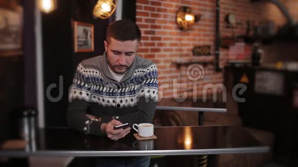 肖像年轻快乐迷人的男人坐在咖啡馆里用电话酒吧里坐着智能手机的帅哥视频的预览图