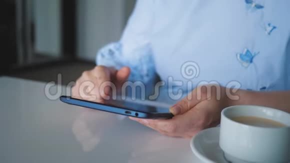 一个年轻的女孩坐在一张桌子旁手里拿着一杯咖啡一块数字平板电脑翻阅着目录视频的预览图