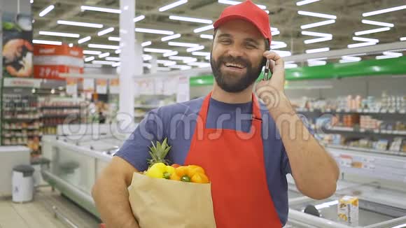 穿着红色制服的帅哥与移动电话交谈手里拿着带蔬菜的购物袋视频的预览图