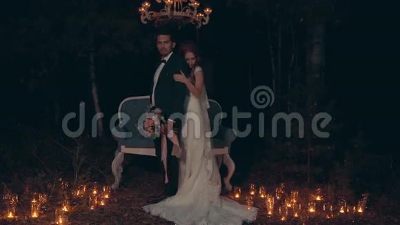 新郎和新娘在夜晚拥抱和亲吻站在黑暗森林的沙发前视频的预览图