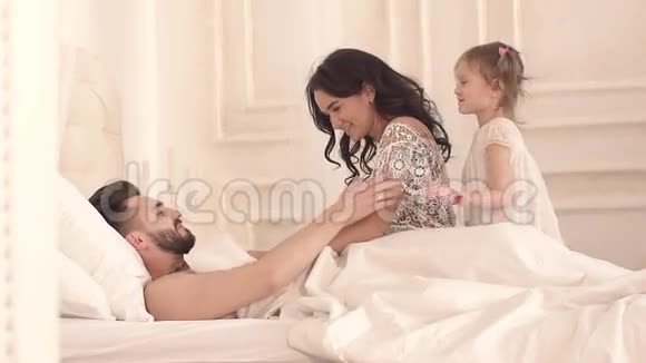 快乐的年轻母亲和小女儿在阳光明媚的早晨叫醒父亲视频的预览图