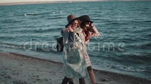 无忧无虑的女朋友在日落时沿着海滩散步享受温暖的秋夜两个穿秋装的女孩玩得很开心视频的预览图
