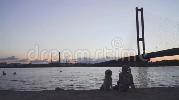 美丽的女孩正和一只狗坐在河岸上视频的预览图