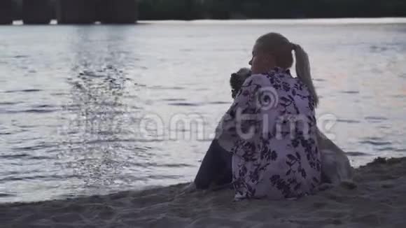美丽的女孩正和一只狗坐在河岸上视频的预览图
