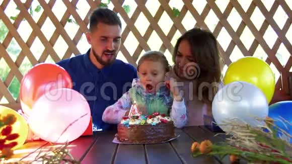快乐的小女孩在生日蛋糕上吹灭蜡烛她慈爱的父母亲吻她拍手视频的预览图