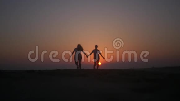 两个朋友牵着手在日落时跳在海滩上高清1920x1080慢动作视频的预览图