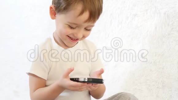 孩子在白色背景上玩智能手机微笑着特写镜头视频的预览图