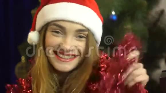 戴着圣诞帽的快乐年轻女孩带着Tinsel笑着看着镜头视频的预览图