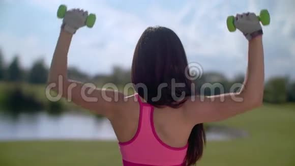 适合女性在户外举重在公园里用哑铃锻炼的女人的背部视频的预览图