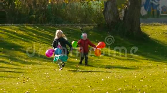 两个可爱的女孩在绿色草地上奔跑手里拿着五颜六色的气球视频的预览图