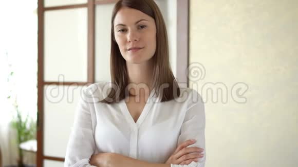 站在客厅微笑的双臂交叉着一幅穿着白色上衣的年轻美女的画像视频的预览图